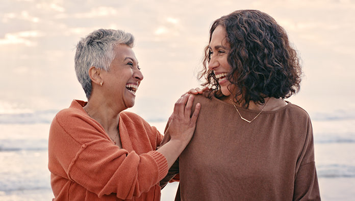 Two woman laughing and smiling while standing on a beach Two woman laughing and smiling while standing on a beach